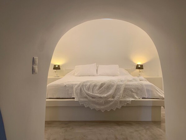 A bedroom with a white bed, two bedside lamps, and a white knitted blanket. - Imer Villas (Santorini)