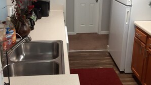 A kitchen with wooden cabinets, a white refrigerator, a stainless steel sink, and a red rug. - Master's apartment rental (Augusta)