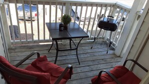 A wooden deck with a table and chairs, a grill, and a view of parked cars. - Master's apartment rental (Augusta)