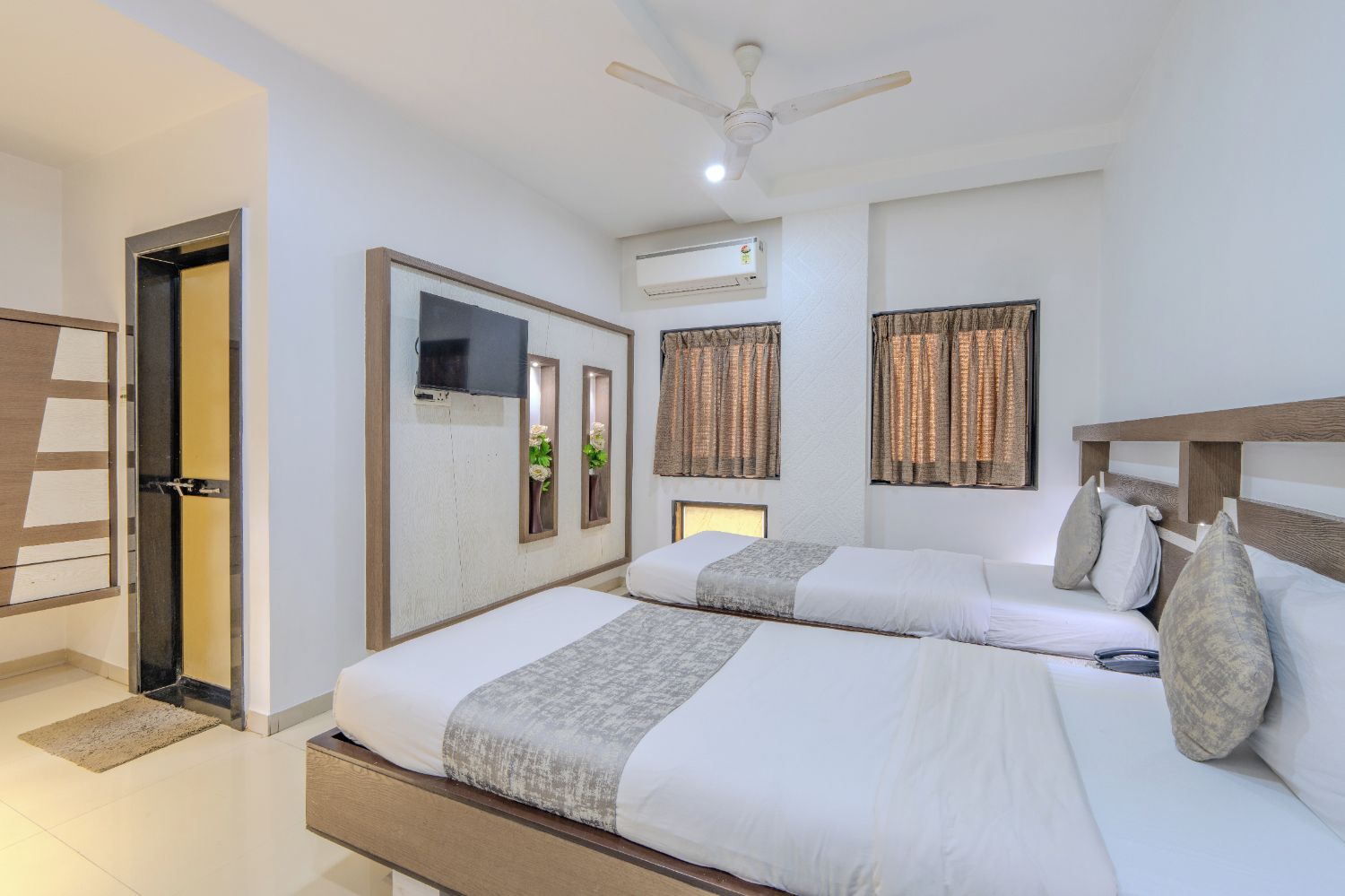 Habitación de hotel con dos camas, ventilador de techo, unidad de aire acondicionado y puerta con espejo.