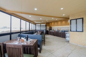 A restaurant with a long counter, seating area, and a view of the water. - Hotel Merit (Surat)