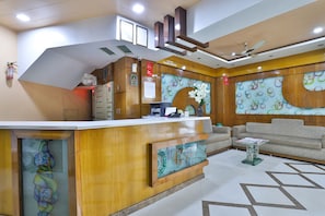 A reception area with a wooden reception desk, a sofa, and a patterned wall. - Hotel Merit (Surat)