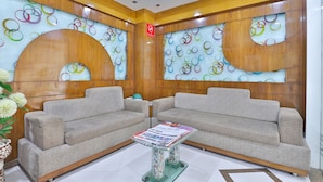 A modern living room with two grey sofas, a glass coffee table, and a wall decorated with colorful circular patterns. - Hotel Merit (Surat)