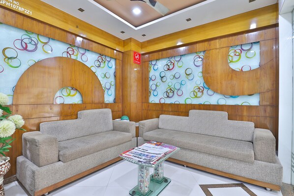 A modern living room with two grey sofas, a glass coffee table, and a wall decorated with colorful circular patterns. - Hotel Merit (Surat)