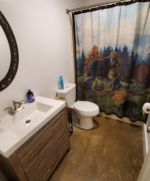 A bathroom with a sink, toilet, and a shower curtain depicting a forest scene.