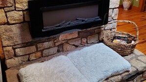 Une cheminée en pierre avec un écran noir, un tapis blanc et moelleux, et un panier en osier rempli de livres.