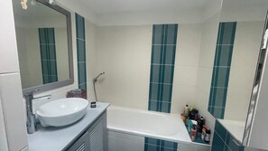 Een badkamer met een wit wastafelmeubel, een spiegel en een bad.