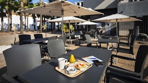 Un café al aire libre con mesas, sillas, sombrillas y una bandeja con comida y una taza.