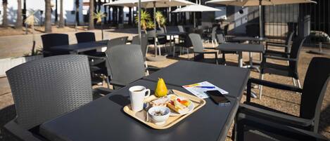 An outdoor cafe with tables and chairs, umbrellas, and a tray with food and a cup.