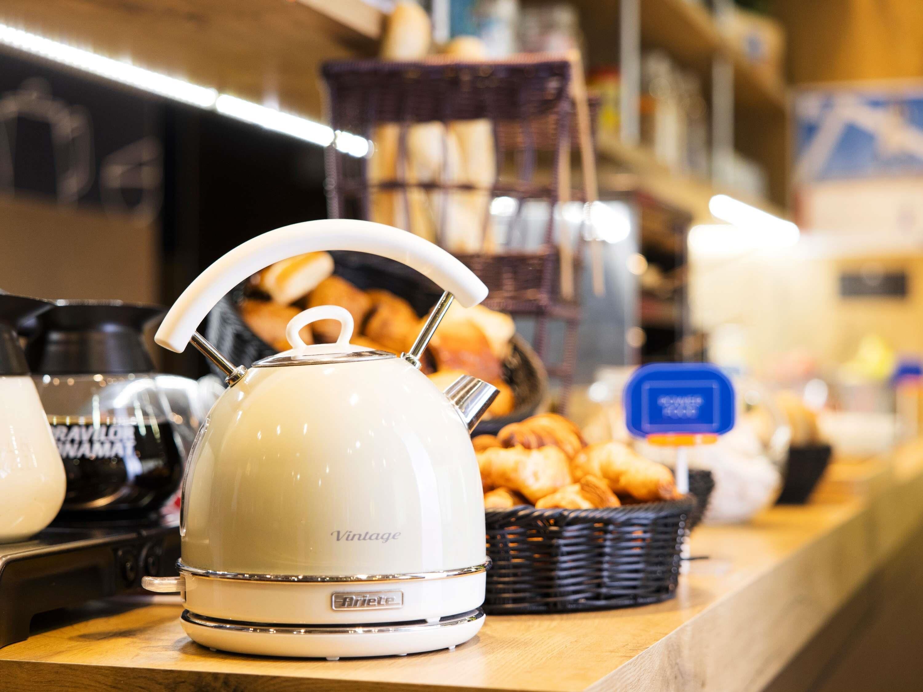 Una cocina con un hervidor de estilo vintage sobre una encimera, una cesta de pasteles y una cafetera.