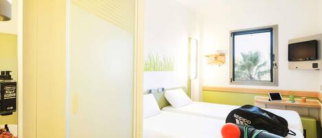 A hotel room with a bed, a desk with a computer, a TV, and a window with a view of palm trees.