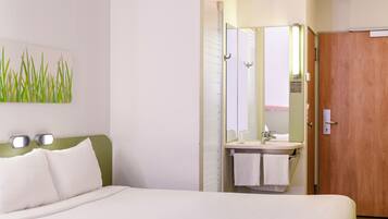 Une chambre d’hôtel avec un lit, une salle de bain comprenant un lavabo et un miroir, et une porte.