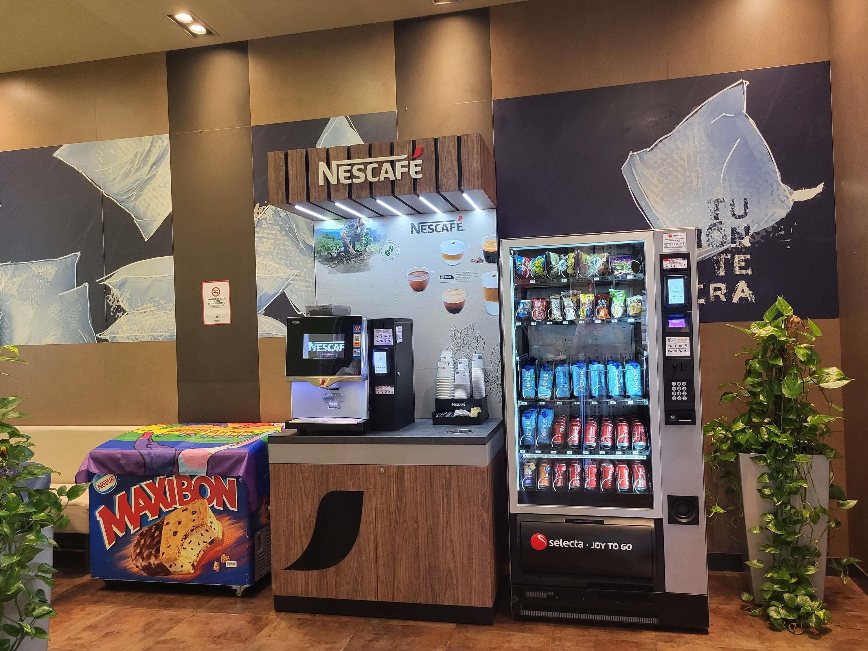 Una estación de café Nescafé, una máquina expendedora de bebidas y una exhibición de snacks Maxibon en un ambiente moderno.