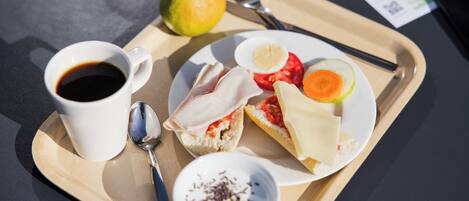 A tray with a cup of coffee, a pear, a sandwich, a slice of tomato, a slice of cucumber, a small bowl of chocolate shavings, and a fork and spoon.