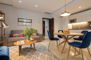 Una sala moderna con sofá, mesa de centro y sillas, un comedor con una mesa redonda y sillas, y una cocina con armarios y microondas.