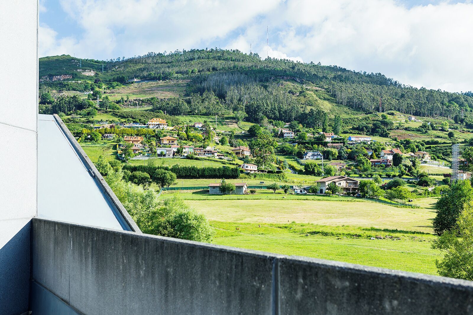Vecindario residencial con casas en una ladera, cielo despejado y una estructura de hormigón en primer plano.