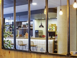 Een restaurant met een bar, zitplaatsen en een keuken op de achtergrond.