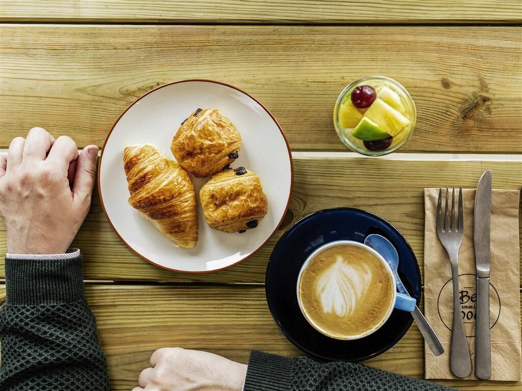 A wooden table with croissants, a fruit cup, and a cup of coffee.