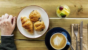 A wooden table with croissants, a fruit cup, and a cup of coffee.