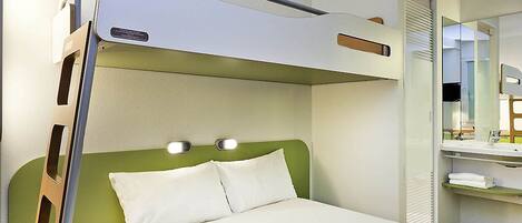 Una cama nido con cabecera verde, una mesita de noche con una botella y un espejo sobre la cama.