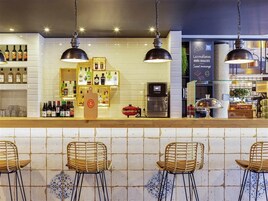 Zona de bar con paredes de azulejos, lámparas colgantes y taburetes.