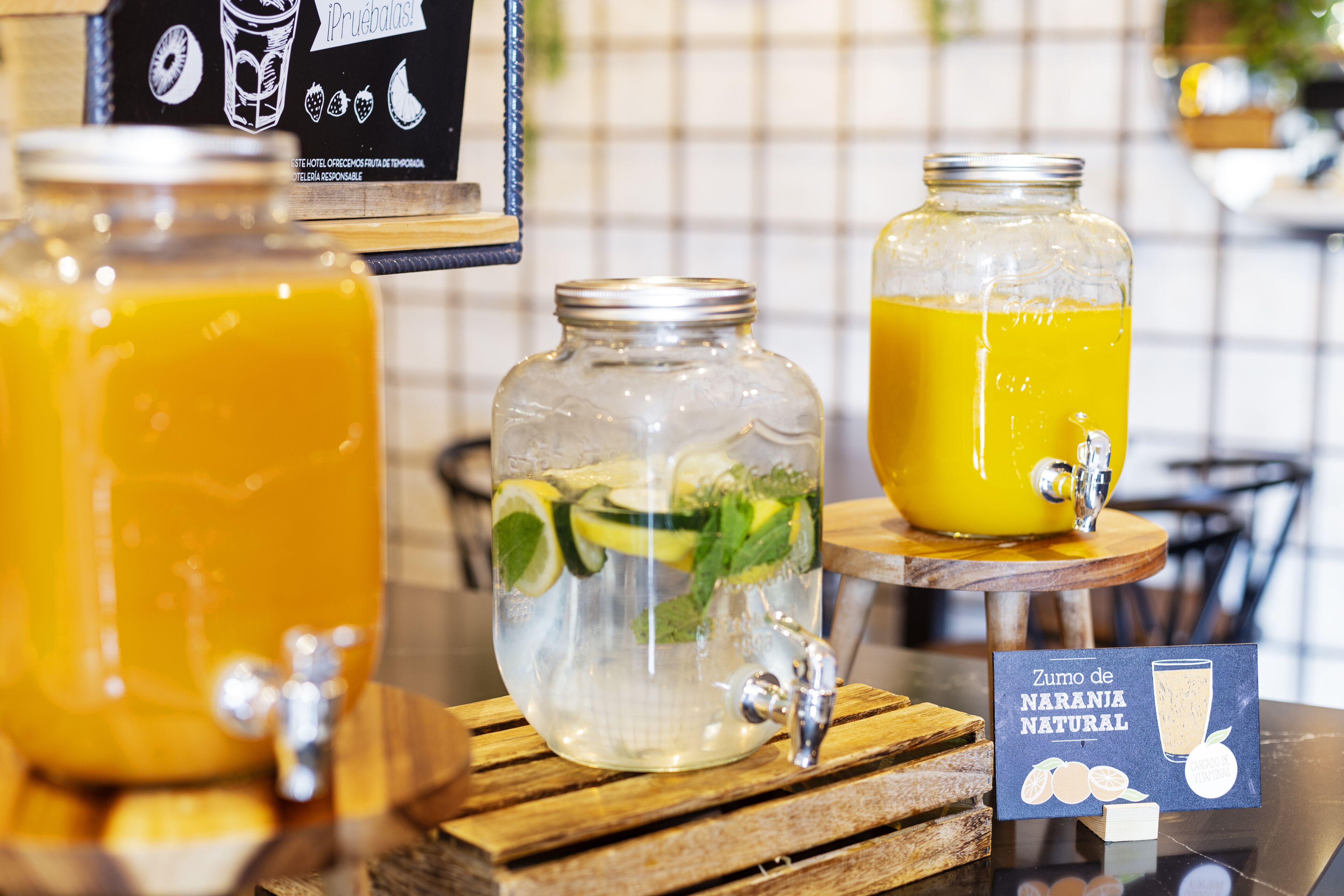 Two glass jars with drinks, one with a tap and mint leaves, and a sign with fruit illustrations.