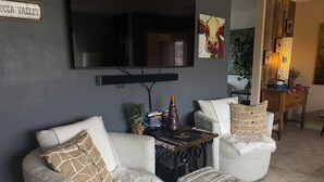 Sala de estar com sofá cinza, banquinho branco e mesa de centro com livros e um objeto decorativo.