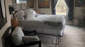 Um quarto com cama, uma cadeira, ventilador de teto e obras de arte nas paredes.