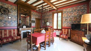 A dining room with a wooden table, chairs, a sofa, and a television. - Mansion and fishing pond near Bergerac (Ginestet)