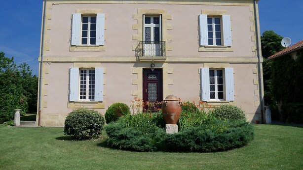 A two-story building with a symmetrical facade, a central entrance with a red door, and a small balcony with decorative railings. - Mansion and fishing pond near Bergerac (Ginestet)