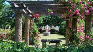A garden with a pergola, stone columns, and a statue in the background. - Mansion and fishing pond near Bergerac (Ginestet)