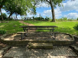 Una mesa de picnic en un parque, con un borde de ladrillo y un césped al fondo.