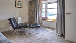 Una habitación con una silla de cuero negro, una pared de piedra, un ventanal y una puerta.