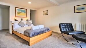 Un dormitorio con una cama de madera, un sillón de cuero negro y dos cuadros en la pared.