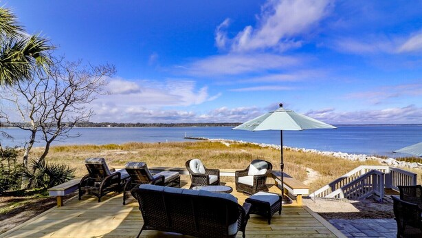 En træterrasse med fletmøbler og en stor parasol med udsigt over stranden.