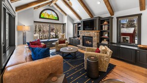 A spacious living room with a fireplace, leather sofa, and a large window overlooking a snowy landscape. - Creekside Hideaway (Crested Butte)