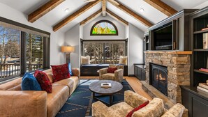A cozy living room with leather sofas, a stone fireplace, a large window, and a fireplace mantel. - Creekside Hideaway (Crested Butte)