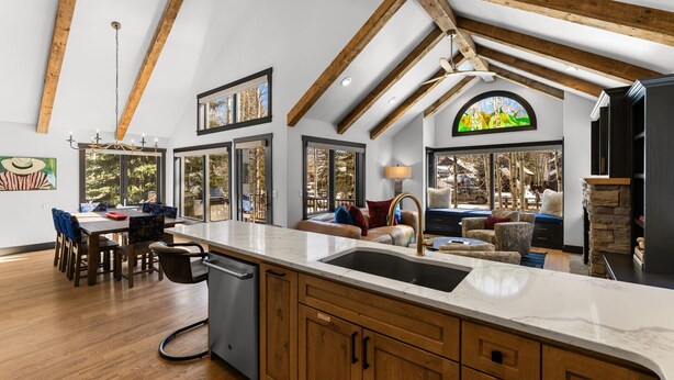 A spacious kitchen with wooden beams, a large island, and a dining area with chairs and a table. - Creekside Hideaway (Crested Butte)