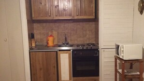 Een functionele keuken met houten kastjes, een vaatwasser, oven en magnetron op een klein tafeltje.