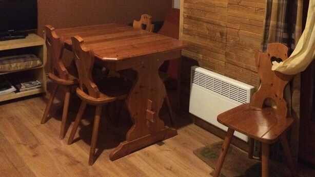 Un comedor con una mesa y sillas de madera, un televisor sobre un mueble bajo y un cuadro en la pared.