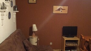 Una sala de estar con un sofá marrón, un televisor sobre un soporte de madera, una lámpara y una mesita.