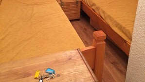 Una habitación pequeña y acogedora con dos camas de madera, una mesita de noche de madera y un cajón pequeño.