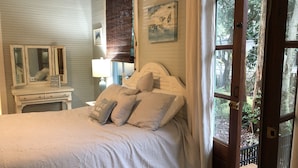 A bedroom with a bed, a dresser, a mirror, and a window with a view of the outdoors. - Old Town Charm ~ Step Back In Time ~ Walk To The Beach (Bay St Louis)