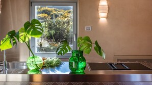 Eine Küchenarbeitsfläche mit zwei grünen Glasvasen mit Pflanzen, ein Fenster mit Blick auf Bäume und eine wandmontierte Leuchte.