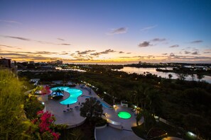 A resort with a large swimming pool, palm trees, and a view of the city at sunset. - Modern Penthouse with amazing view- Private Pool (Cupecoy)
