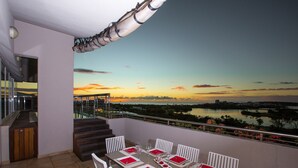 A dining area with a table set for six, white chairs, and a view of a sunset over a body of water. - Modern Penthouse with amazing view- Private Pool (Cupecoy)