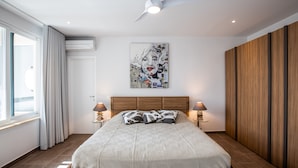 A modern bedroom with a large bed, two bedside lamps, a ceiling fan, and a large window with curtains. - Modern Penthouse with amazing view- Private Pool (Cupecoy)