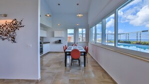 A modern kitchen with white cabinets, a dining area with a table and chairs, and large windows with a view of the sea. - Modern Penthouse with amazing view- Private Pool (Cupecoy)