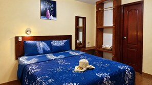 A bed with a blue floral bedspread, a wooden headboard, and a wall-mounted light. - Hostal Mariscal Sucre (Tababela)