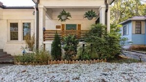 Una casa amb un porxo cobert, una escala i un petit jardí amb plantes i una tanca de fusta.